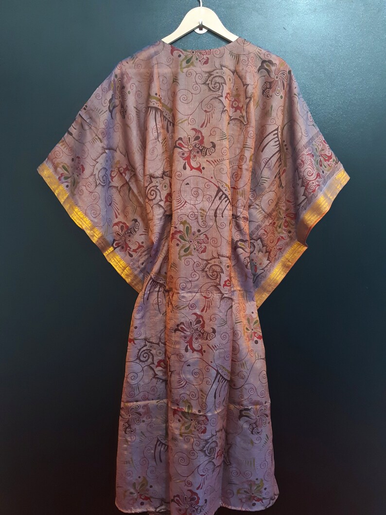 May include: A long, flowing, pink silk robe with a floral pattern and gold trim. The robe has a wide, open neckline and long sleeves.