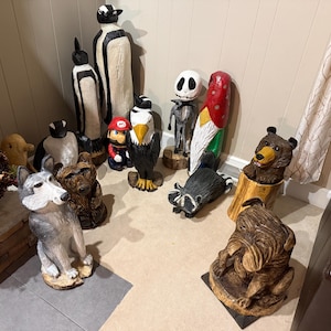 Può includere: Una collezione di sculture di animali in legno intagliato, tra cui un lupo, un orso, un procione, un'aquila e un pinguino. Altre figure includono uno gnomo, Jack Skellington e una statuetta di Mario. Le sculture sono dipinte in vari colori.