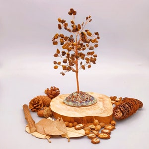 May include: A small tree made of tiger's eye stones and copper wire, sitting on a wooden base with a small pile of pine cones and other natural elements around it.
