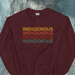 May include: A maroon sweatshirt with the word "INDIGENOUS" repeated four times in a retro, rainbow-colored font.