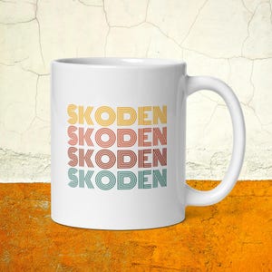 May include: White ceramic mug with the name "SKODIEN" repeated four times in a retro, layered font with orange, yellow, red, and green colors.