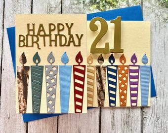 May include: A handmade birthday card with the words "Happy Birthday" and the number "21" in gold glitter. The card features a design of colorful candles with different patterns.