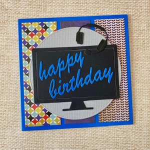 May include: A blue and black birthday card featuring a computer monitor design. The monitor displays a blue "happy birthday" message and has a pair of headphones on top.