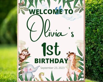 May include: Welcome to Olivia's 1st Birthday sign with a jungle theme. The sign features a green leafy border, a white background, and illustrations of a monkey, elephant, giraffe, and snake. The text "Welcome to Olivia's 1st Birthday" is in green text and the date "September 23, 2023" is in black text.