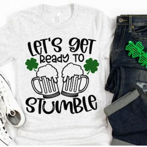May include: A white t-shirt with the text "Let's get ready to stumble" and a graphic of two beer mugs with shamrocks.