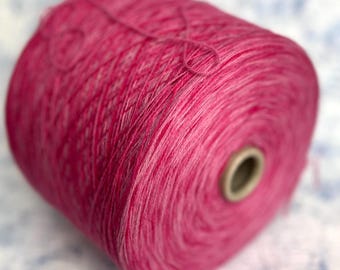 May include: A spool of pink yarn with a white stripe. The yarn is wound tightly around the spool.