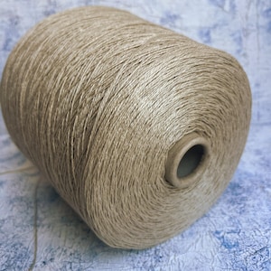 May include: A spool of beige yarn, wound tightly and ready for knitting or crocheting.