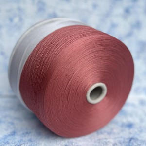 Può includere: Un'bobina di filo di colore rosa scuro avvolta attorno a un nucleo di cartone bianco.
