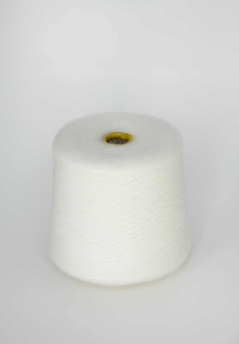 Puede incluir: Un cono de hilo blanco con un agujero central amarillo.