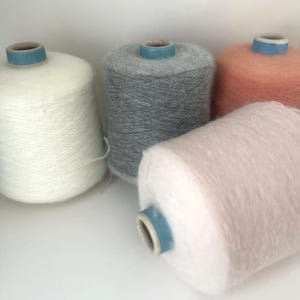 Peut inclure: Gros plan sur cinq bobines de fil de différentes couleurs : blanc, gris, rose clair et pêche. Le fil est duveteux et doux, avec un cœur en carton bleu clair. Idéal pour les projets de tricot et de crochet.