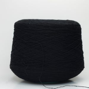 May include: A large, cone-shaped spool of black yarn. The yarn is tightly wound, with a single strand extending from the base. The background is plain white, highlighting the dark colour and texture of the yarn. Suitable for knitting and crochet.