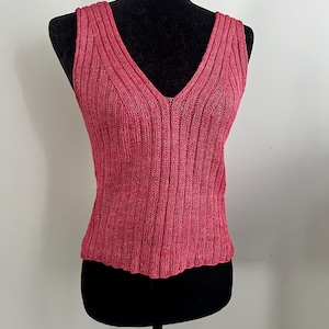May include: A sleeveless pink knitted top with a V-neckline.