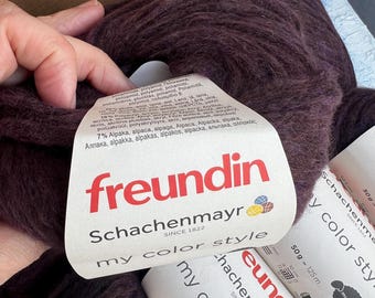 以下が含まれることがあります： 「freundin Schachenmayr my color style」というラベルが付いた、濃い紫色の糸の巻き糸。ラベルには「7% アルパカ、アルパカ、アルパカ、アルパカ、アルパカ、アルパカ、アルパカ、アルパカ、アルパカ、アルパカ、アルパカ、アルパカ、アルパカ」と記載されています。