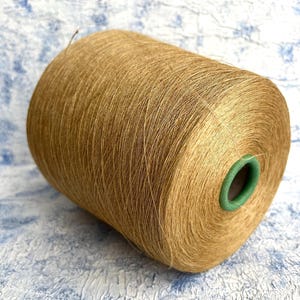 Könnte beinhalten: Eine Spule mit goldbraunem Garn und einem grünen Plastikkern.