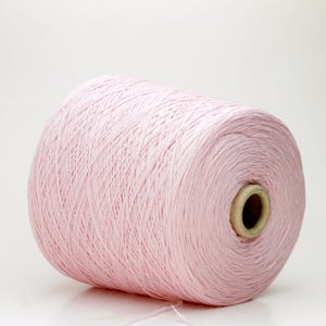 Peut inclure: Une grosse bobine de fil rose clair. Le fil est bien enroulé et a une texture lisse. La bobine a un noyau en carton. Idéal pour le tricot, le crochet ou d'autres projets d'art textile.