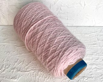May include: A skein of pale pink yarn wound on a cardboard bobbin with a blue plastic end cap.