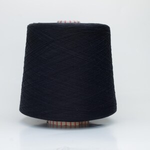 May include: A large, cylindrical cone of solid black yarn. The thread is tightly wound in a cross-hatch pattern around a central plastic spool, which features a ribbed base and top edge. The yarn has a matte texture and uniform dark color.