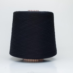 May include: A large, cylindrical cone of solid black yarn. The thread is tightly wound in a cross-hatch pattern around a central plastic spool, which features a ribbed base and top edge. The yarn has a matte texture and uniform dark color.