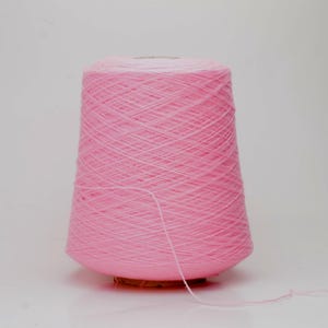 Peut inclure: Une grosse bobine de fil rose, idéale pour les projets de tricot ou de crochet. Le fil est étroitement enroulé, créant une forme conique. Un brin de fil s'étend de la bobine, suggérant qu'il est prêt à l'emploi. Le fond est blanc uni.