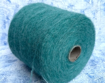 May include: A large spool of teal yarn. The yarn is fluffy and soft, with a slight sheen. The spool has a cardboard core. The yarn is a solid colour, with no visible patterns or variations.