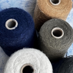 May include: Four spools of yarn in different colors: white, dark blue, gray, and brown. The spools are arranged in a circle.