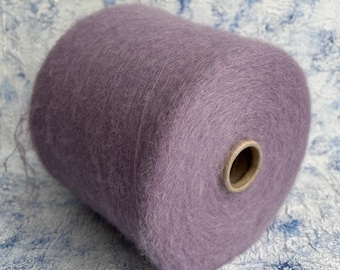 May include: A large spool of lavender yarn. The yarn has a soft, fluffy texture and a subtle sheen. A cardboard core is visible at one end. Suitable for knitting and crochet crafts.
