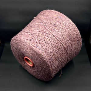 Puede incluir: Un ovillo de hilo malva con motas azules y amarillas. El hilo está enrollado en forma de bola y está listo para tejer o hacer ganchillo.