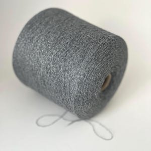 Peut inclure: Une grosse bobine de fil gris avec une surface texturée. Le fil est enroulé serré autour d'un noyau en carton, avec un brin de fil qui s'étend de la bobine. Idéal pour les projets de tricot et de crochet.