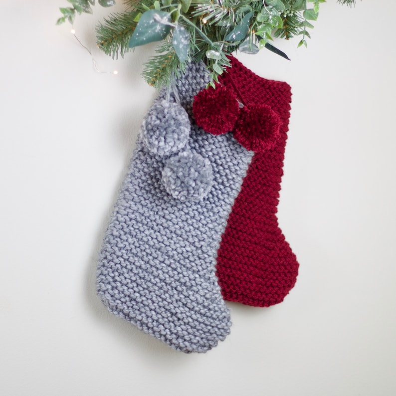 May include: Two knitted Christmas stockings with pom-poms. One stocking is gray and the other is red.
