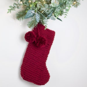 May include: A burgundy knitted Christmas stocking with two fluffy white pom-poms.