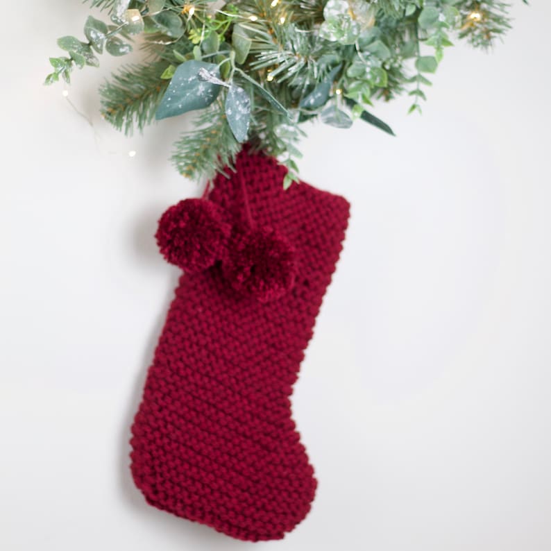 May include: A burgundy knitted Christmas stocking with two fluffy white pom-poms.
