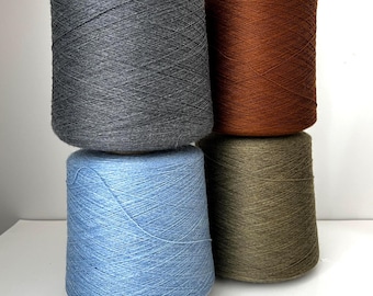 May include: Four spools of yarn in shades of gray, brown, blue, and olive green are stacked. The yarn is tightly wound on conical spools, showcasing the texture and color variations. The arrangement suggests a selection for crafting projects.