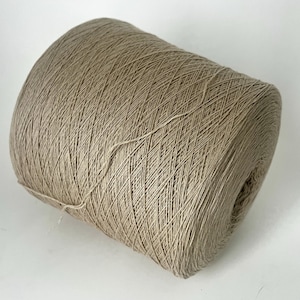 Peut inclure: Une grosse bobine de fil beige, bien enroulée et prête pour le travail manuel. Le fil semble être une fibre naturelle, avec une surface légèrement texturée. La bobine est cylindrique, avec le fil soigneusement superposé.