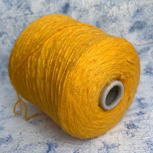 May include: A skein of bright yellow yarn, wound into a ball shape. The yarn is soft and fluffy, and it is perfect for knitting or crocheting.