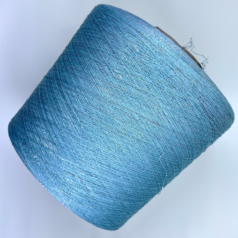 May include: A skein of light blue yarn with a subtle shimmer. The yarn is wound into a cone shape.