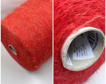 May include: A skein of bright orange yarn with a fuzzy texture. The yarn is labeled "Hair-Plane" with the text "TIT. NM9000, COL. 2405, LOT# H206397, 50% PAR 50% WP, CYCLED CARTON".