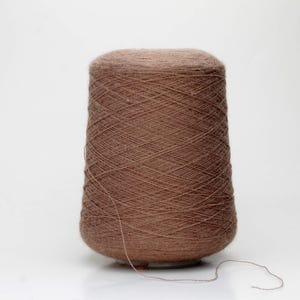 May include: A brown yarn cone, ideal for knitting and crochet projects. The yarn is a warm, earthy tone, and the cone shape is clearly visible against a white background. A strand of yarn extends from the cone.
