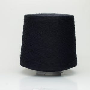 May include: A large cone of black yarn, suitable for knitting or crocheting, is centered against a white background. The yarn is tightly wound, creating a smooth, dark surface. The cone sits on a small, light-colored base.