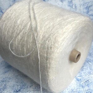 May include: A skein of white yarn with a fuzzy texture. The yarn is wound around a cardboard tube.