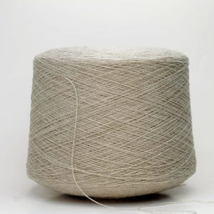 May include: A large, cylindrical spool of light grey yarn. The yarn is tightly wound, creating a textured surface. A single strand of yarn extends from the spool, suggesting it's ready for use in knitting or crochet projects.