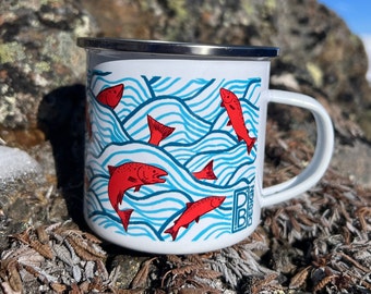 May include: White enamel mug with a silver rim, featuring a design of red fish swimming in blue wavy lines. The mug has a white handle and the letters "PB DESIGN" are printed on the side.