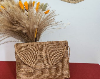 Może przedstawiać: Brązowa pleciona torebka typu kopertówka z klapką. Torebka wykonana jest z naturalnych materiałów i ma rustykalny, boho styl.