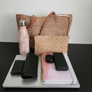 May include: A collection of everyday carry items, including a woven tote bag with leather handles, a matching clutch, a pink floral water bottle, a laptop, a notebook, a power bank, a wallet, and wireless earbuds. The items are arranged on a black surface.