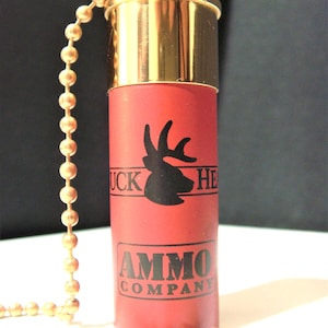Könnte beinhalten: Eine rote und goldene Schrotflinten-Zugkette mit einer schwarzen Hirsch-Silhouette und dem Text "Duck Head Ammo Company".