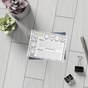 May include: A white card with a decorative border and text, including "Concentration," "Description," and "Level." The card is on a stack of blue cards, with a pen and binder clips nearby. Two small potted succulents are in the background.