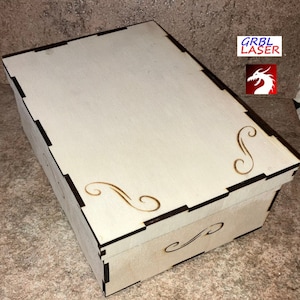 May include: A wooden box with a light brown finish and intricate laser-cut designs. The box has a hinged lid and a decorative flourish on the front.