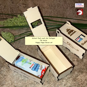 K&ouml;nnte beinhalten: Zwei Holzkisten mit ge&ouml;ffneten Deckeln, die eine Schokoladentafel im Inneren zeigen. Die Kisten sind mit einem Kuchen und den Worten "Happy Hippo Boxen" und "Birthday!" verziert. Die Kisten sind aus hellem Holz und haben eine nat&uuml;rliche Oberfl&auml;che.