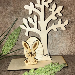 May include: Wooden Easter bunny and tree cutout with a base. The bunny is sitting in an egg and the tree has many branches.