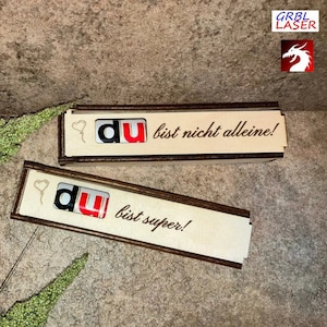 Könnte beinhalten: Zwei Holzkisten mit braunem Rand. Die obere Kiste hat den Text "du bist nicht alleine!" und die untere Kiste hat den Text "du bist super!" Beide Kisten haben eine kleine Herzform und das Wort "du" in Rot und Weiß.