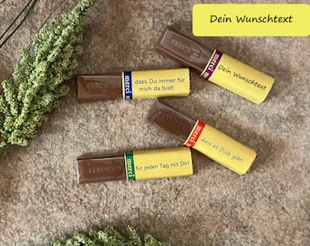 May include: Four chocolate bars wrapped in yellow paper with the word "merci" printed on them. Each bar has a different message written on it in German. The messages are: "dass Du immer für mich da bist!" (that you are always there for me!), "dass es Dich gibt!" (that you exist!), "für jeden Tag mit Dir!" (for every day with you!), and "Dein Wunschtext" (your desired text).